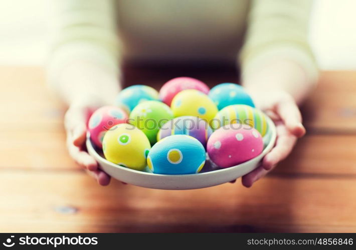 easter, holidays, tradition and people concept - close up of woman hands holding colored easter eggs on plate