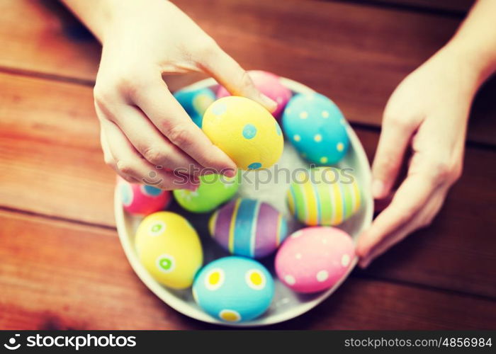 easter, holidays, tradition and people concept - close up of woman hands with colored easter eggs on plate