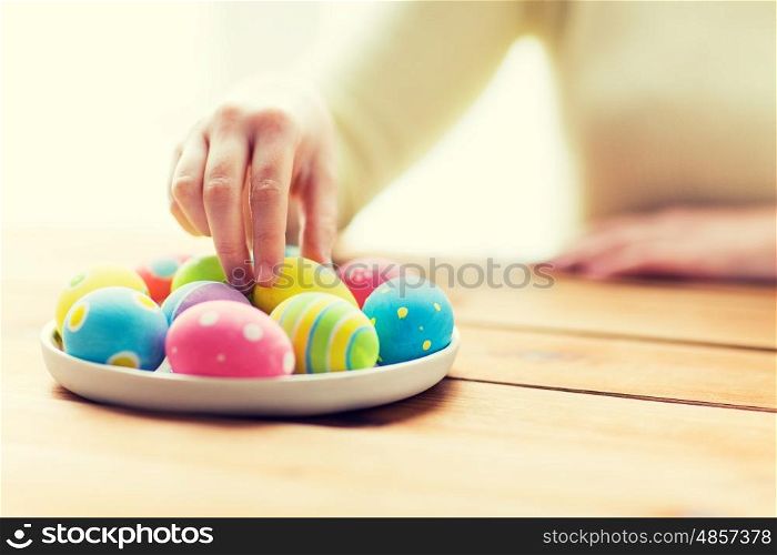 easter, holidays, tradition and people concept - close up of woman hands with colored easter eggs on plate