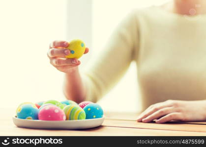 easter, holidays, tradition and people concept - close up of woman hands with colored easter eggs on plate