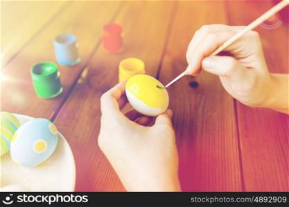 easter, holidays, tradition and people concept - close up of woman hands coloring easter eggs with colors and brush