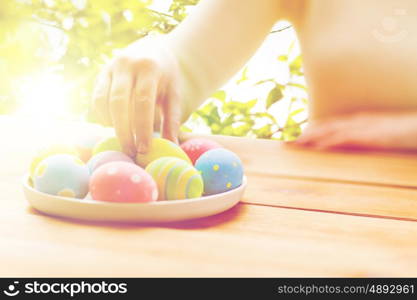 easter, holidays, tradition and people concept - close up of woman hands with colored easter eggs on plate