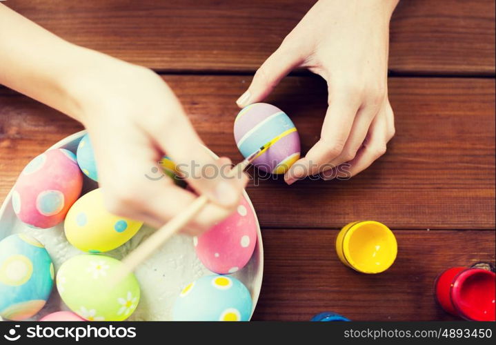 easter, holidays, tradition and people concept - close up of woman hands coloring easter eggs with colors and brush