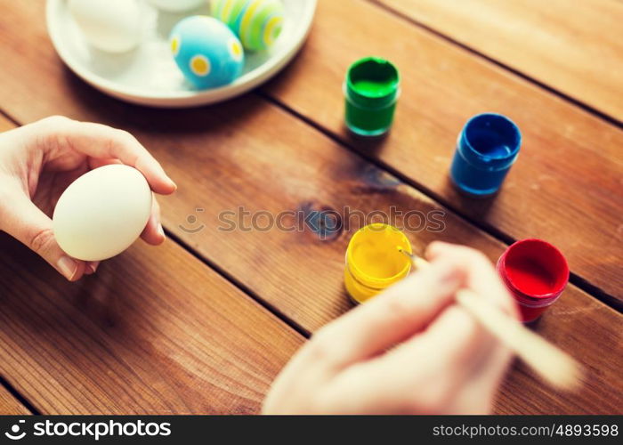 easter, holidays, tradition and people concept - close up of woman hands coloring easter eggs with colors and brush