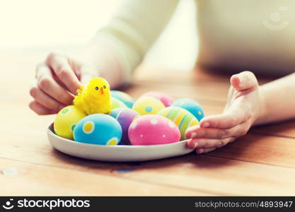 easter, holidays, tradition and people concept - close up of woman hands with colored easter eggs on plate