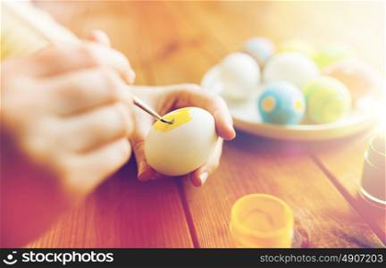 easter, holidays, tradition and people concept - close up of woman hands coloring easter eggs with colors and brush. close up of woman hands coloring easter eggs