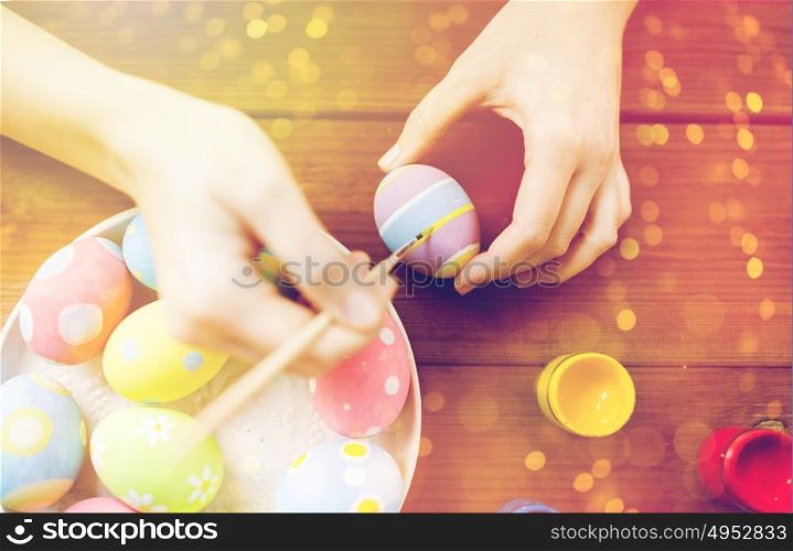 easter, holidays, tradition and people concept - close up of woman hands coloring easter eggs with colors and brush. close up of woman hands coloring easter eggs