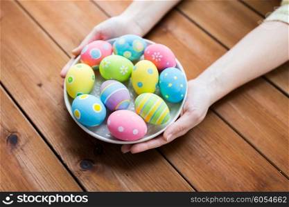 easter, holidays, tradition and people concept - close up of woman hands holding colored easter eggs on plate