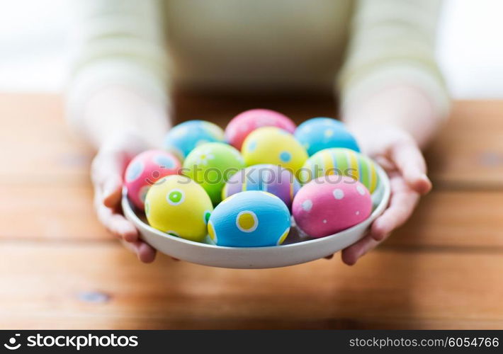 easter, holidays, tradition and people concept - close up of woman hands holding colored easter eggs on plate