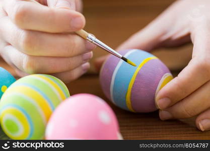 easter, holidays, tradition and people concept - close up of woman hands coloring easter eggs with brush