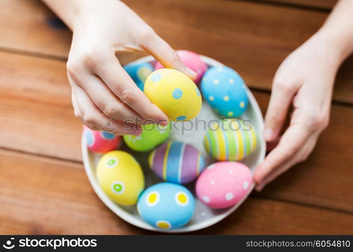 easter, holidays, tradition and people concept - close up of woman hands with colored easter eggs on plate