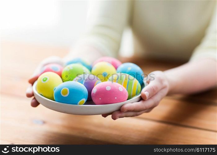 easter, holidays, tradition and people concept - close up of woman hands holding colored easter eggs on plate