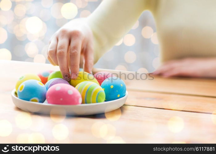 easter, holidays, tradition and people concept - close up of woman hands with colored easter eggs on plate