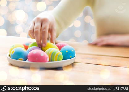 easter, holidays, tradition and people concept - close up of woman hands with colored easter eggs on plate