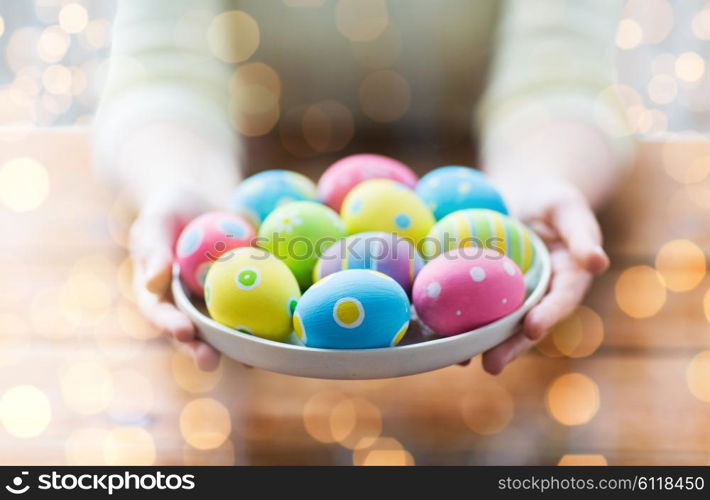 easter, holidays, tradition and people concept - close up of woman hands holding colored easter eggs on plate