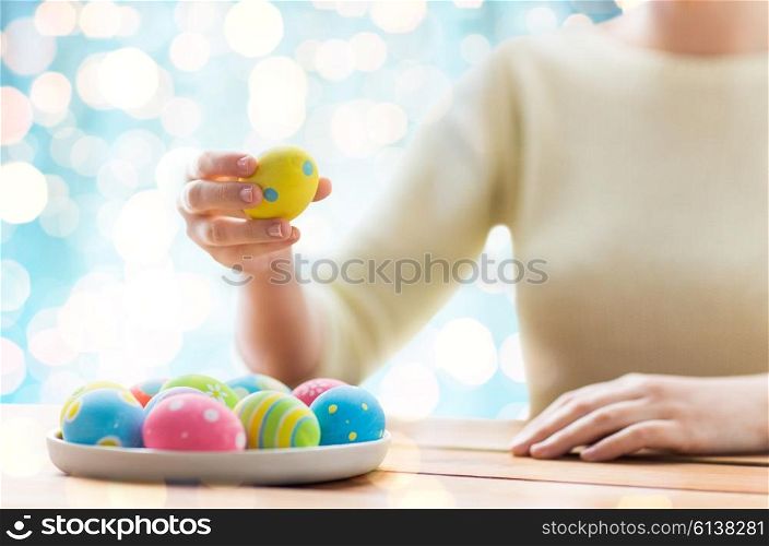 easter, holidays, tradition and people concept - close up of woman hands with colored easter eggs on plate