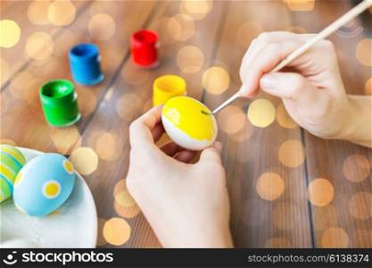 easter, holidays, tradition and people concept - close up of woman hands coloring easter eggs with colors and brush