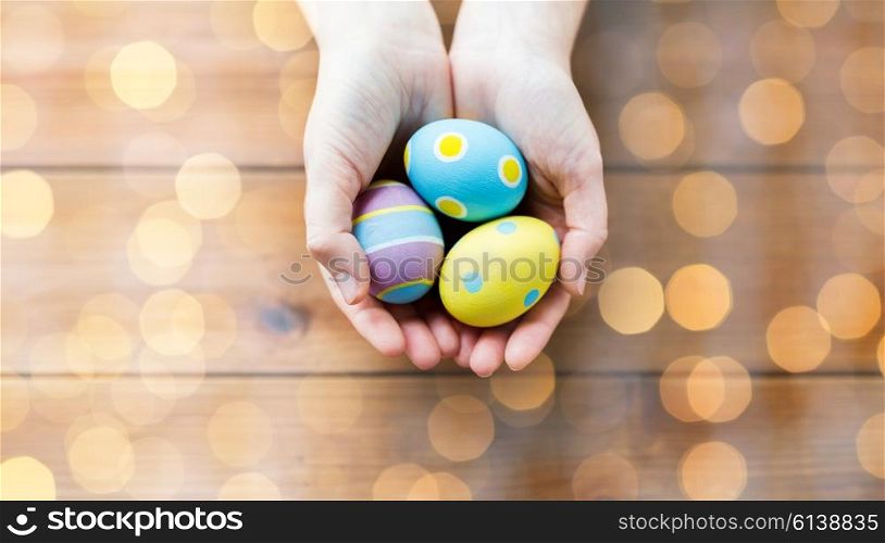 easter, holidays, tradition and people concept - close up of woman hands holding colored easter eggs over holidays lights