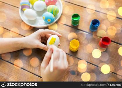 easter, holidays, tradition and people concept - close up of woman hands coloring easter eggs with colors and brush over lights