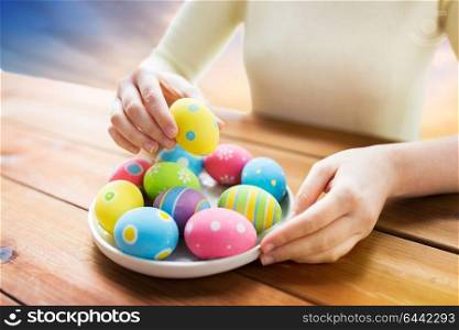 easter, holidays, tradition and people concept - close up of woman hands with colored eggs on plate over sky background. close up of woman hands with colored easter eggs