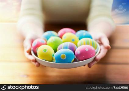 easter, holidays, tradition and people concept - close up of woman hands holding colored eggs on plate over sky background. close up of woman hands with colored easter eggs