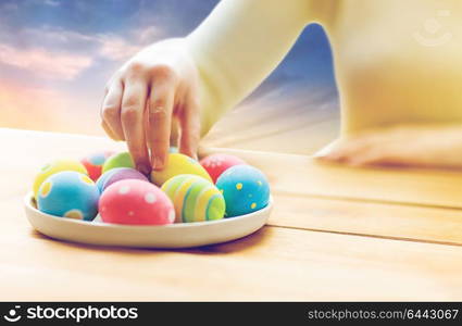 easter, holidays, tradition and people concept - close up of woman hands with colored eggs on plate over sky background. close up of woman hands with colored easter eggs