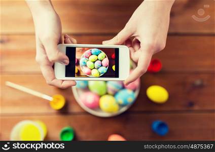 easter, holidays, tradition, technology and people concept - close up of woman hands with smartphone taking picture of colored easter eggs
