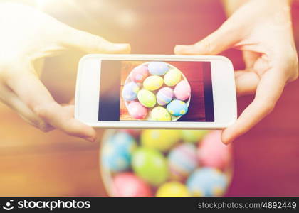 easter, holidays, tradition, technology and people concept - close up of woman hands with smartphone taking picture of colored easter eggs