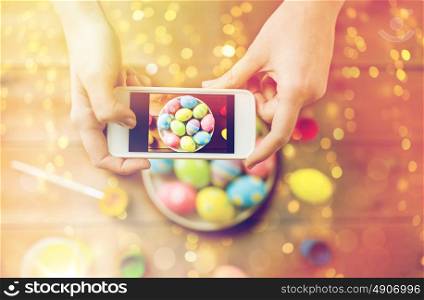 easter, holidays, tradition, technology and people concept - close up of woman hands with smartphone taking picture of colored easter eggs. close up of hands with easter eggs and smartphone