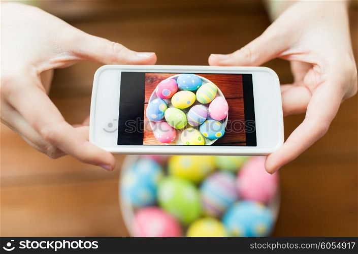 easter, holidays, tradition, technology and people concept - close up of woman hands with smartphone taking picture of colored easter eggs