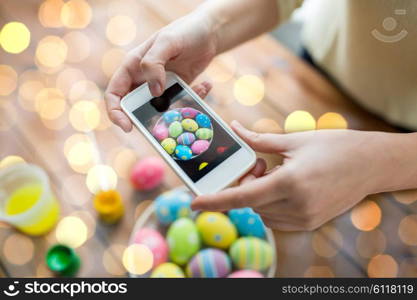 easter, holidays, tradition, technology and people concept - close up of woman hands with smartphone taking picture of colored easter eggs