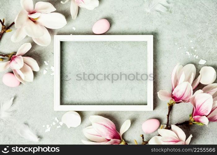 Easter mock up with Photo frame, space for text, beautiful spring magnolia flowers and Easter decorations on grey stone background. Flat lay, top view, copy space