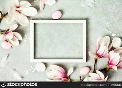 Easter mock up with Photo frame, space for text, beautiful spring magnolia flowers and Easter decorations on grey stone background. Flat lay, top view, copy space
