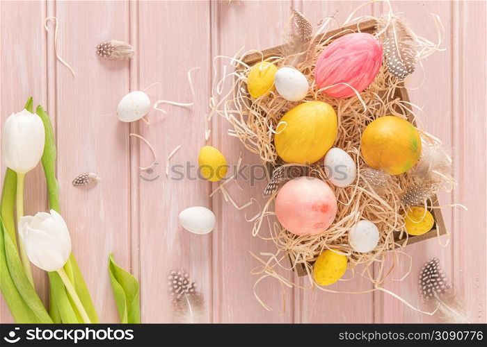 Easter pink, yellow and white eggs in wooden box and white tulips