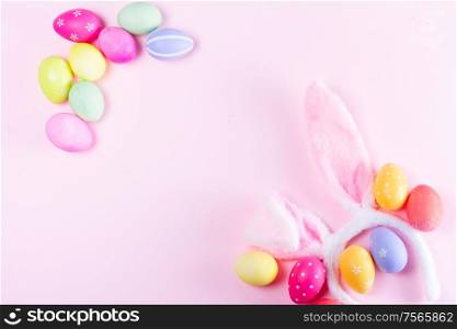 Easter rabbit flaffy ears and colored easter colored eggs frame on pink plain background, flat lay with copy space. Easter scene with rabbit ears