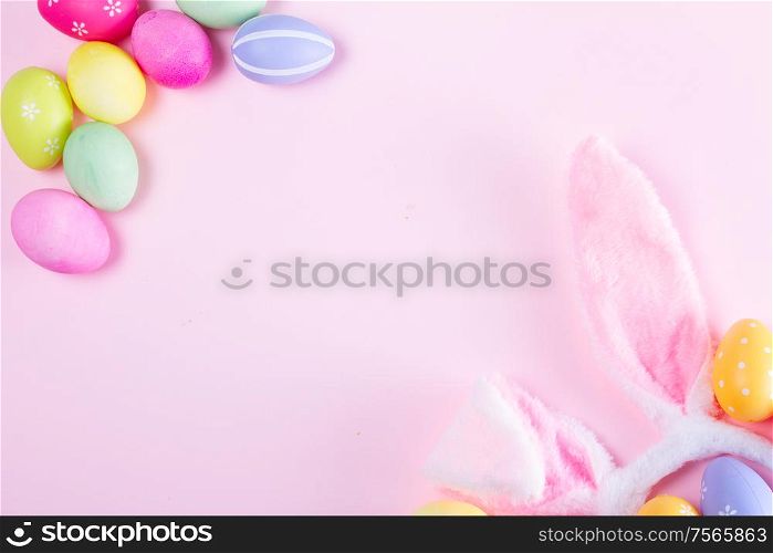 Easter rabbit flaffy ears and colored easter colored eggs frame on pink background, flat lay with copy space. Easter scene with rabbit ears