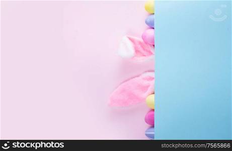 Easter rabbit flaffy ears and colored easter colored eggs on pink and blue background banner with copy space. Easter scene with rabbit ears