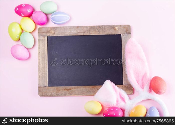 Easter rabbit flaffy ears and colored easter colored eggs on pink background with copy space on blackboard. Easter scene with rabbit ears