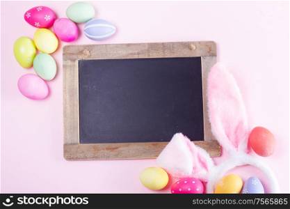 Easter rabbit flaffy ears and colored easter colored eggs on pink background with copy space on blackboard. Easter scene with rabbit ears