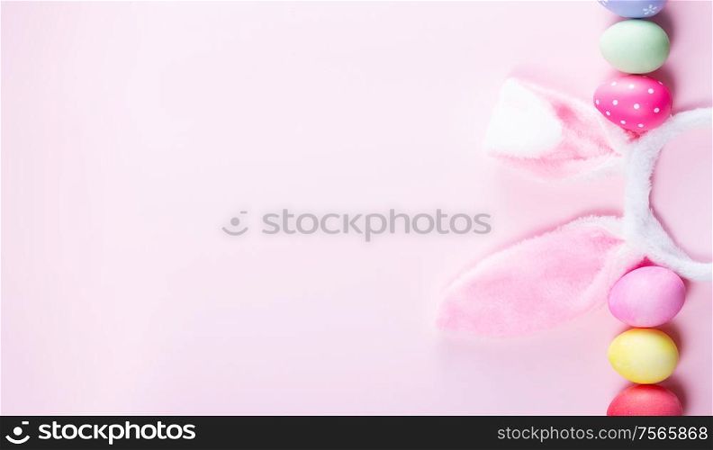 Easter rabbit flaffy ears and colored easter colored eggs on pink background banner with copy space. Easter scene with rabbit ears