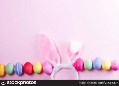 Easter rabbit flaffy ears and colored easter colored eggs on pink background with copy space. Easter scene with rabbit ears
