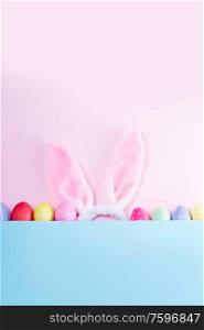 Easter rabbit flaffy ears and colored easter colored eggs, top view flat lay on pink and blue plain minimal background with copy space. Easter scene with rabbit ears