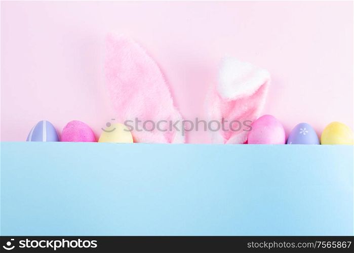 Easter rabbit flaffy ears and colored easter colored eggs, top view on pink and blue plain background with copy space. Easter scene with rabbit ears