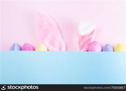 Easter rabbit flaffy ears and colored easter colored eggs, top view on pink and blue plain background with copy space. Easter scene with rabbit ears