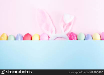 Easter rabbit flaffy ears and colored easter colored eggs, top view on pink and blue plain minimal background with copy space. Easter scene with rabbit ears