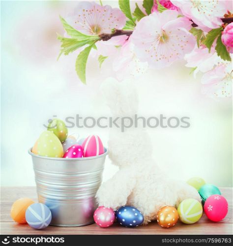 easter rabbit with metal pot full of eggs on blue background, retro toned. egg hunt with easter bunny