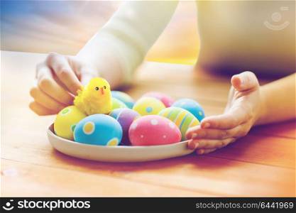 easter, religious holidays and people concept - close up of woman hands with colored eggs and toy chicken on plate over sky background. close up of woman hands with colored easter eggs