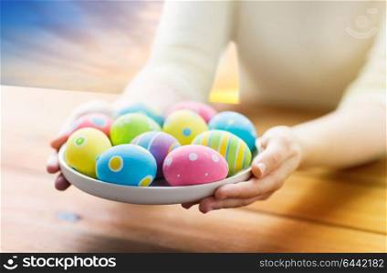 easter, religious holidays and people concept - close up of woman hands with colored eggs on plate over sky background. close up of woman hands with colored easter eggs