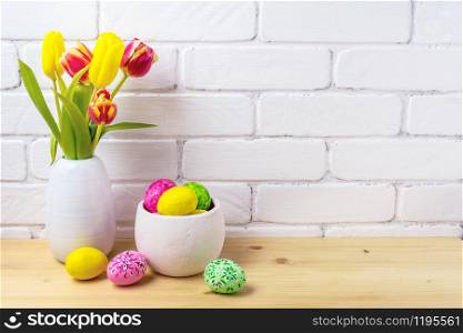 Easter rustic arrangement with decorated eggs, red and yellow tulips in the white vase near painted brick wall