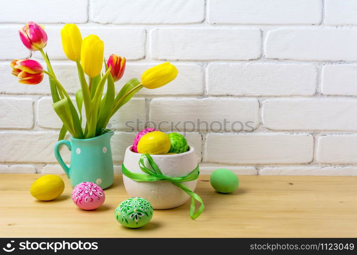 Easter rustic centerpiece with decorated eggs, green ribbon, red and yellow tulips in the polka dot mint green jug near painted brick wall